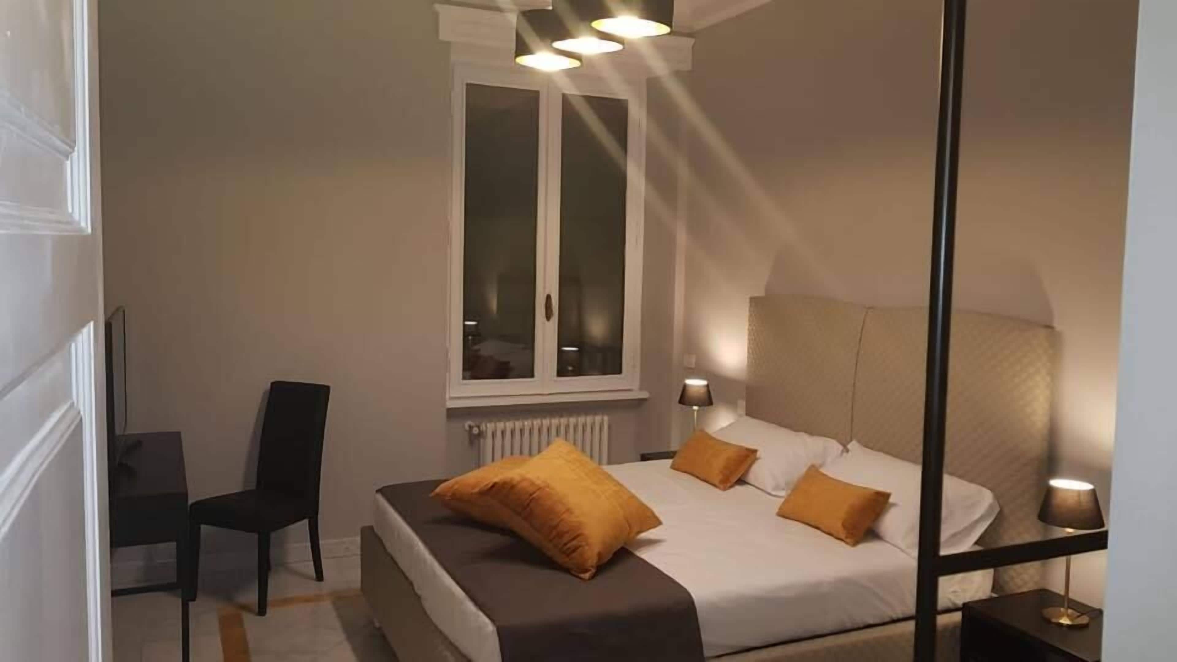 Une chambre à coucher avec un lit, deux lampes de chevet, une fenêtre, un radiateur et une chaise.