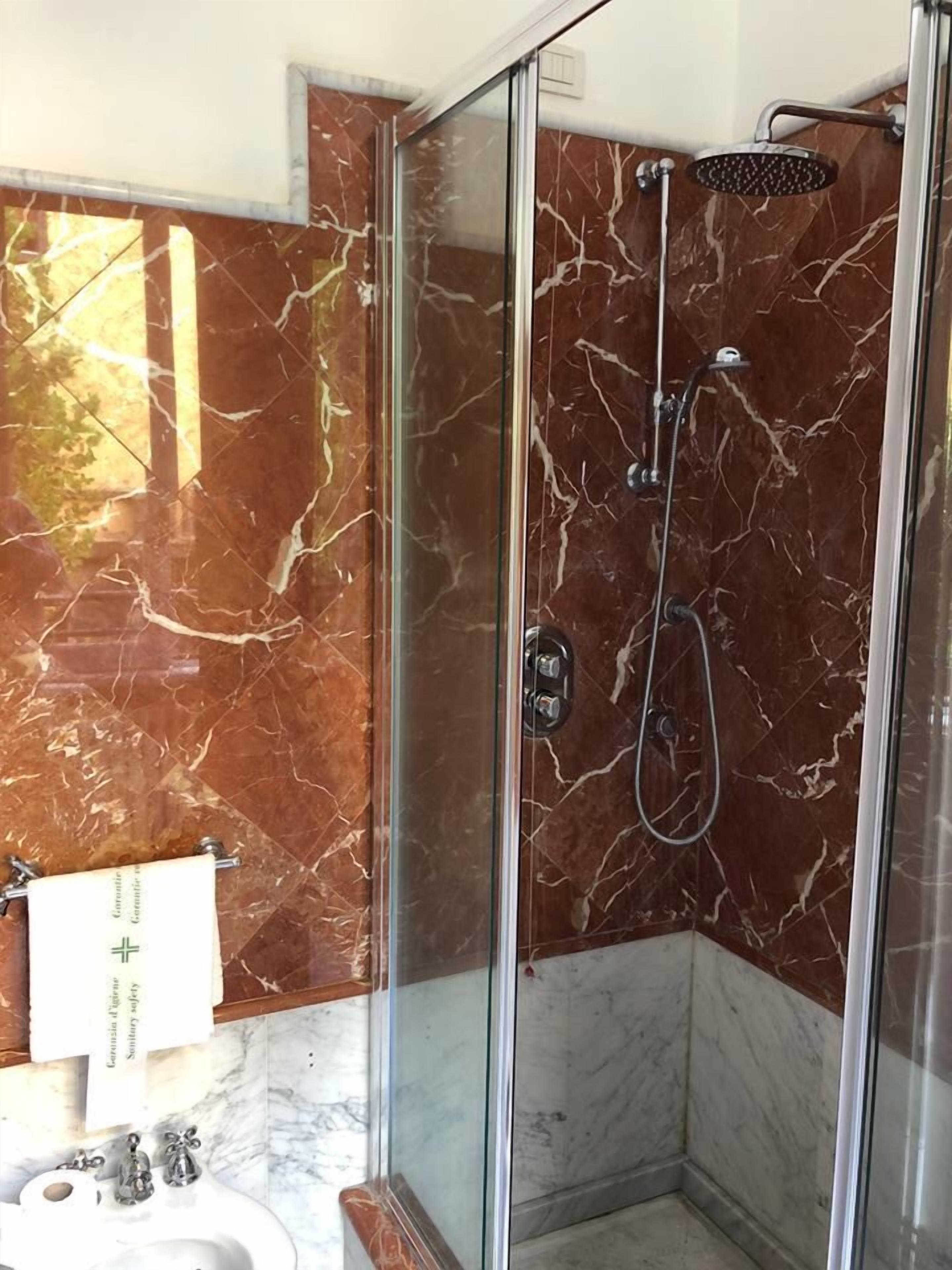 Une salle de bain moderne avec une douche à parois de verre, des murs en marbre et un lavabo blanc.