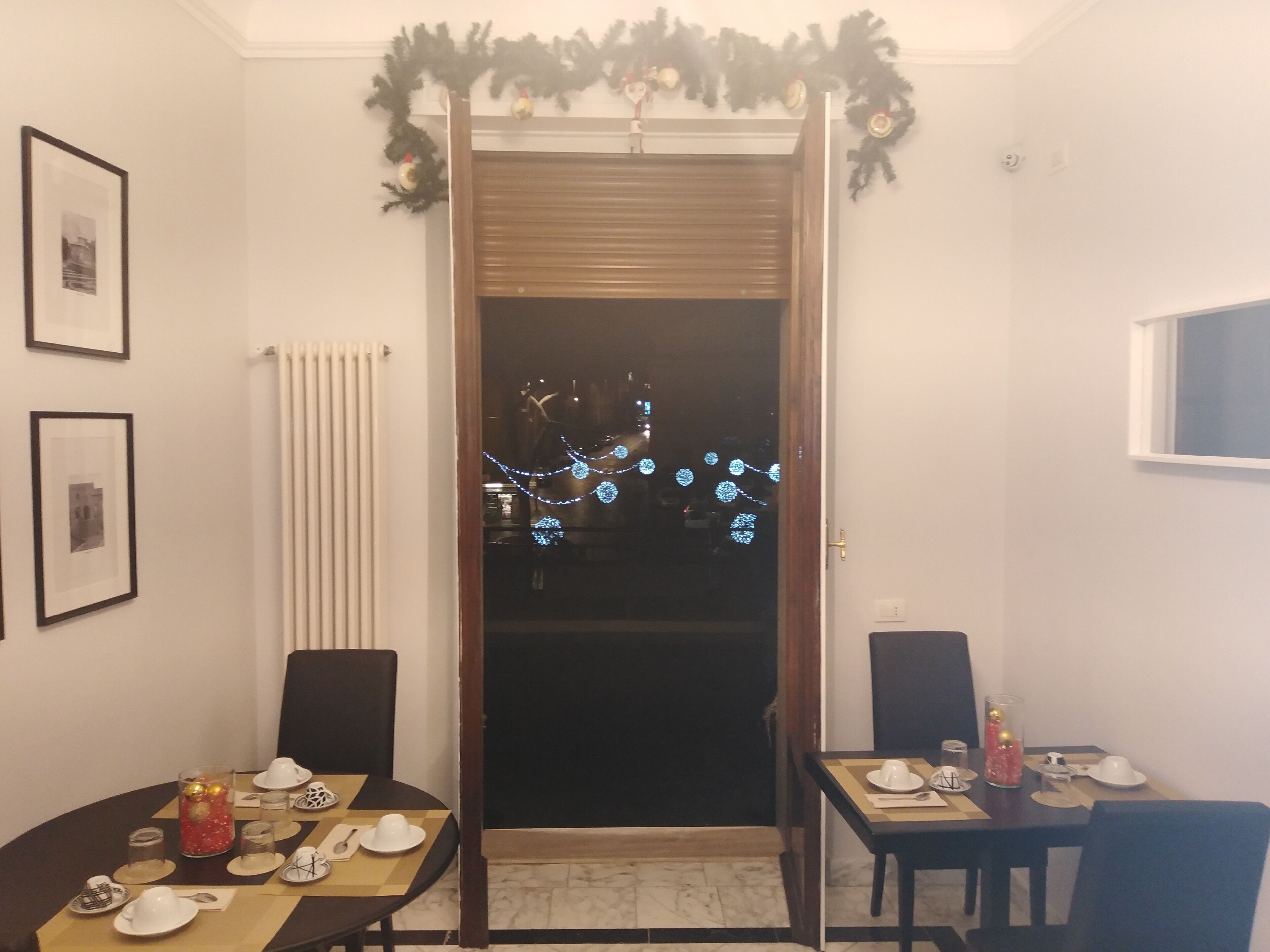 Un coin repas avec deux tables dressées pour le repas, un radiateur, des tableaux encadrés au mur et une porte décorée pour les fêtes.