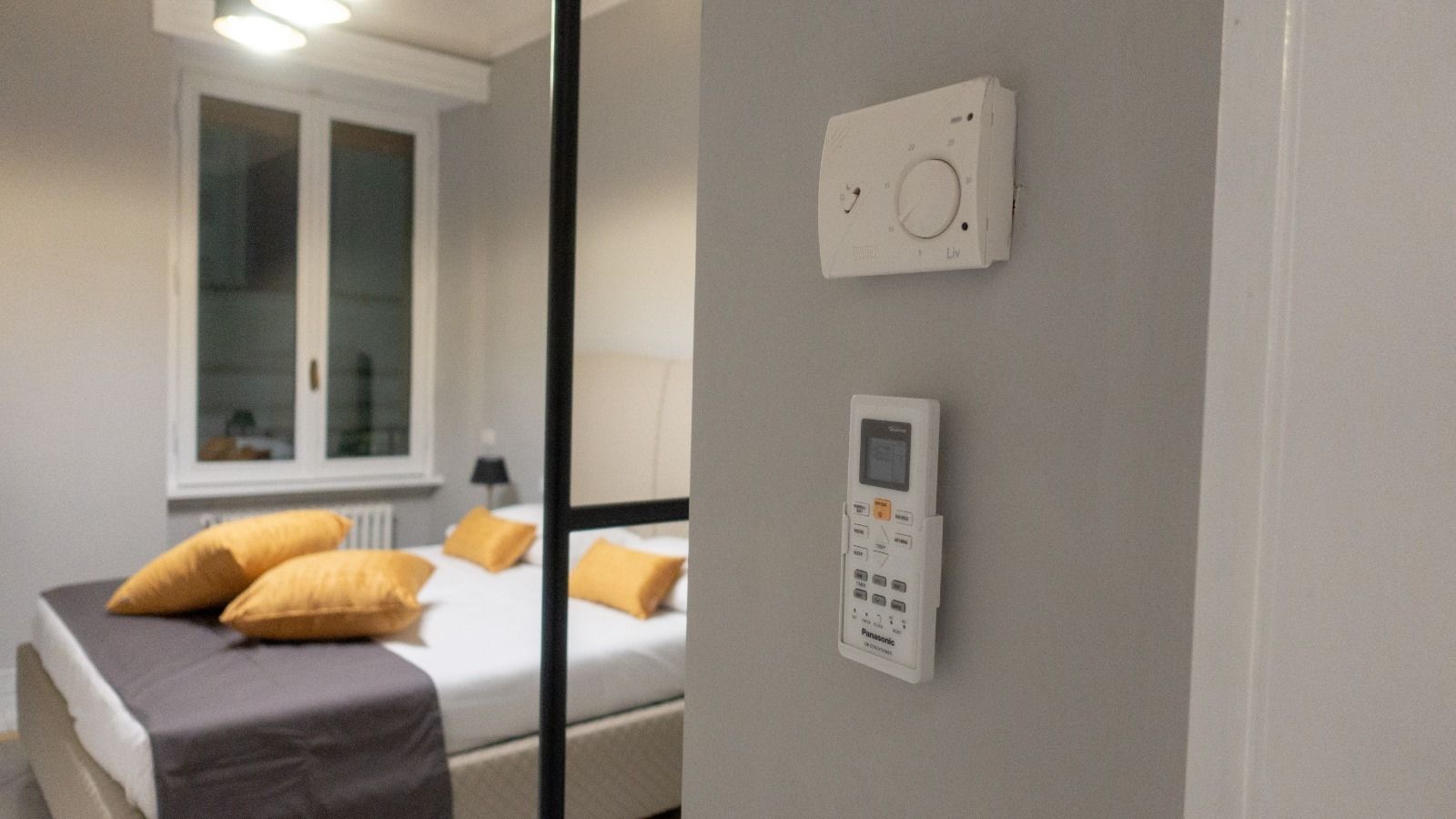 Un dormitorio con cama, almohadas, un panel de control en la pared y una ventana.
