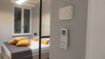 Un dormitorio con cama, almohadas, un panel de control en la pared y una ventana.