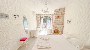 Quarto com uma cama grande, um banquinho pequeno, um espelho, uma lareira e vista para o exterior.