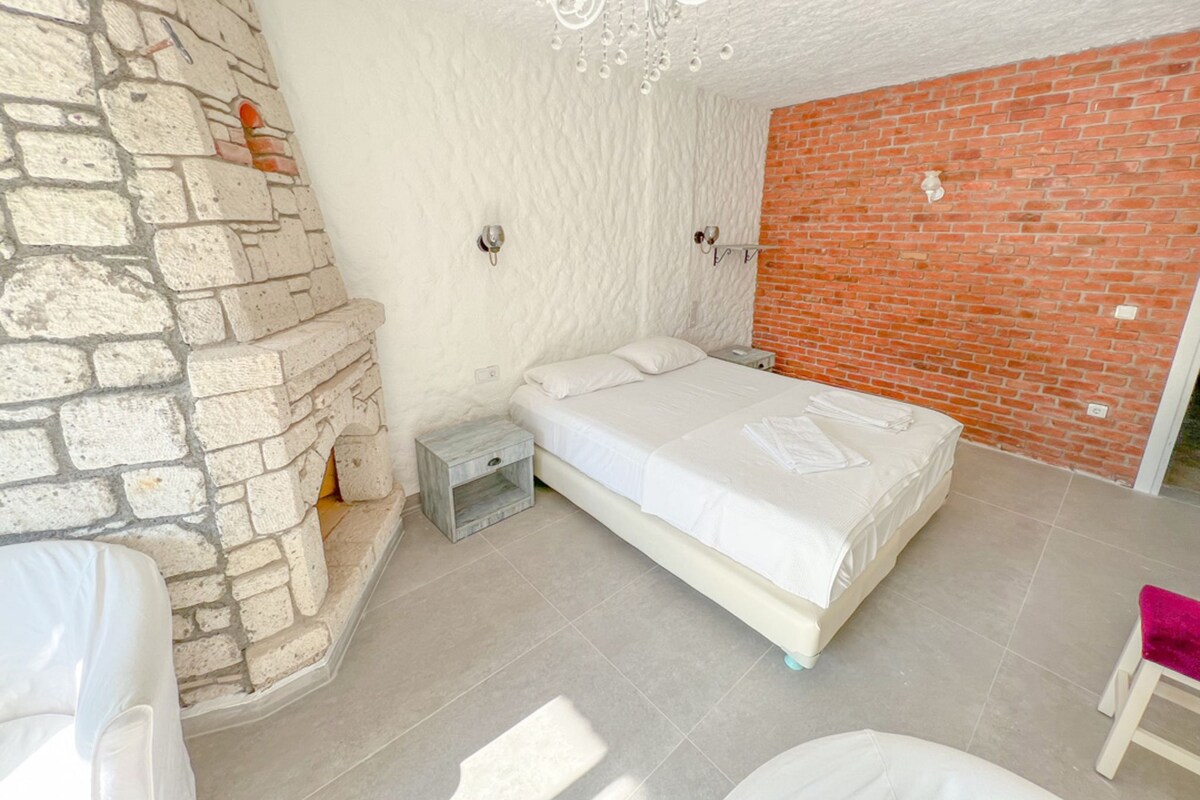 A bedroom with a stone wall, a brick wall, a bed, a nightstand, and a chandelier.