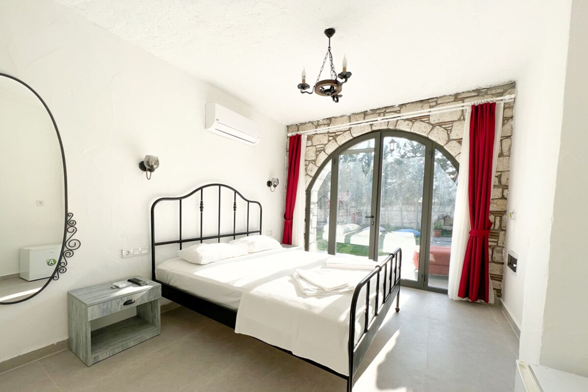 A bedroom with a bed, a nightstand, a wardrobe, a window with curtains, and a chandelier.
