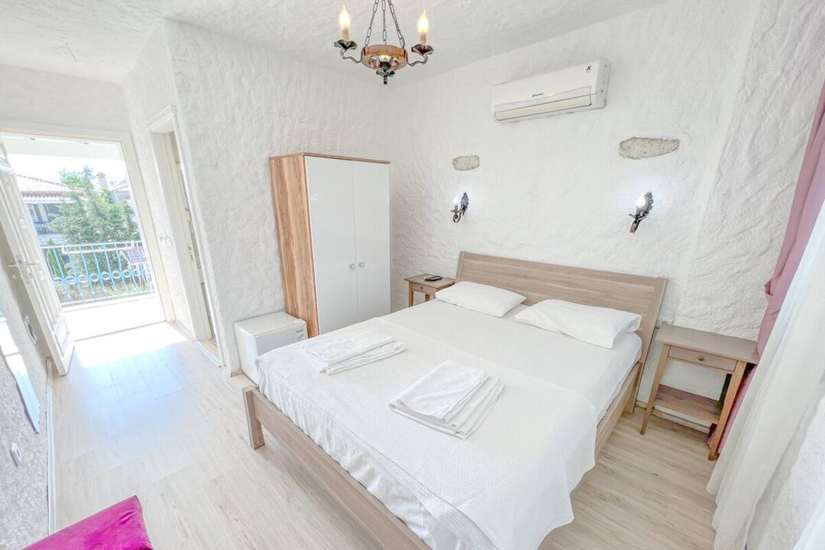 A bedroom with a large bed, a wooden wardrobe, a bedside table, and a hanging light fixture.