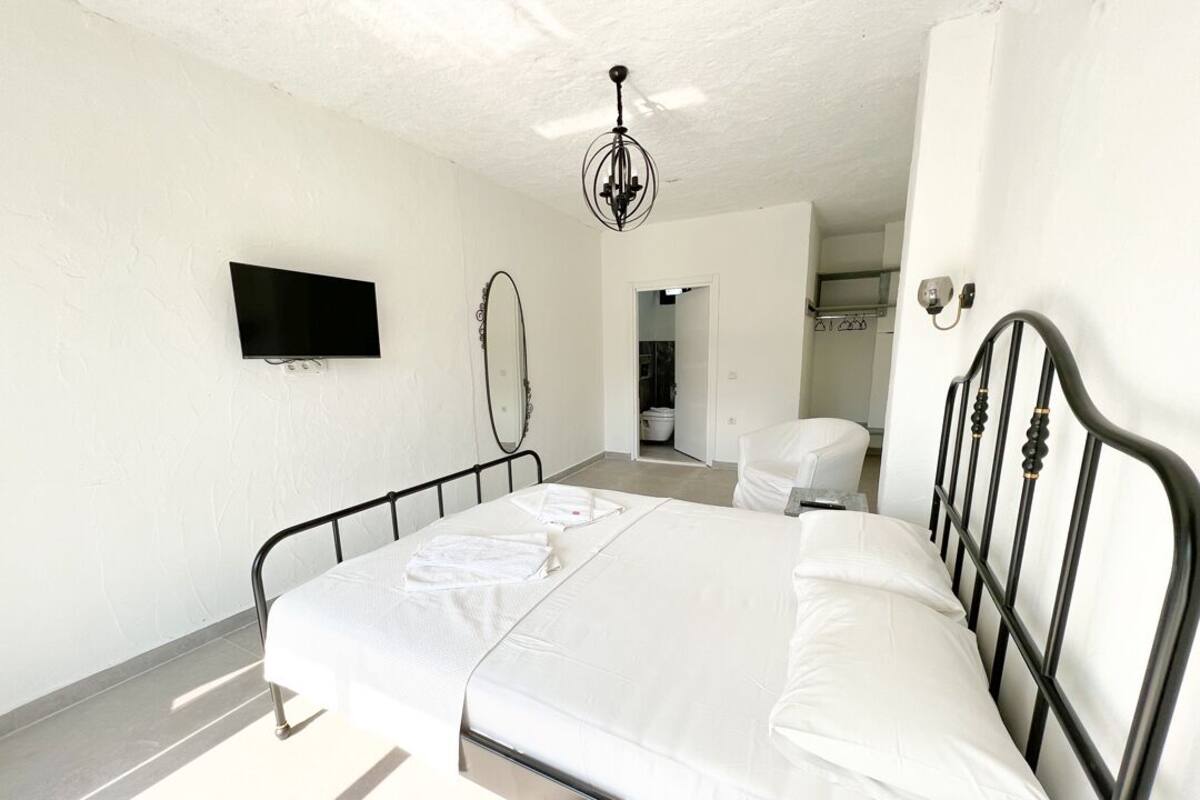 A bedroom with a bed, a TV mounted on the wall, a mirror, and a chandelier.