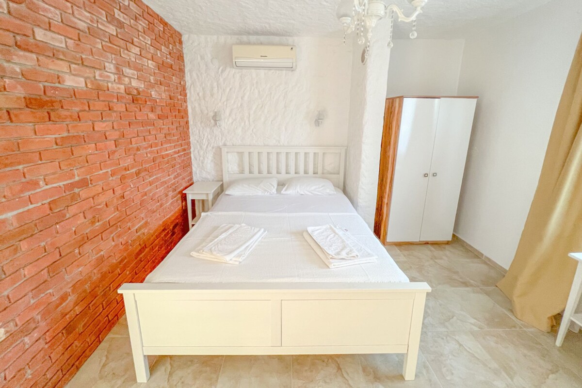 A bedroom with a white bed, a brick wall, a white wardrobe, and a ceiling fan.