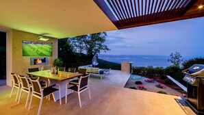 Een moderne eethoek buiten, met een televisiescherm, een barbecue en een prachtig uitzicht.