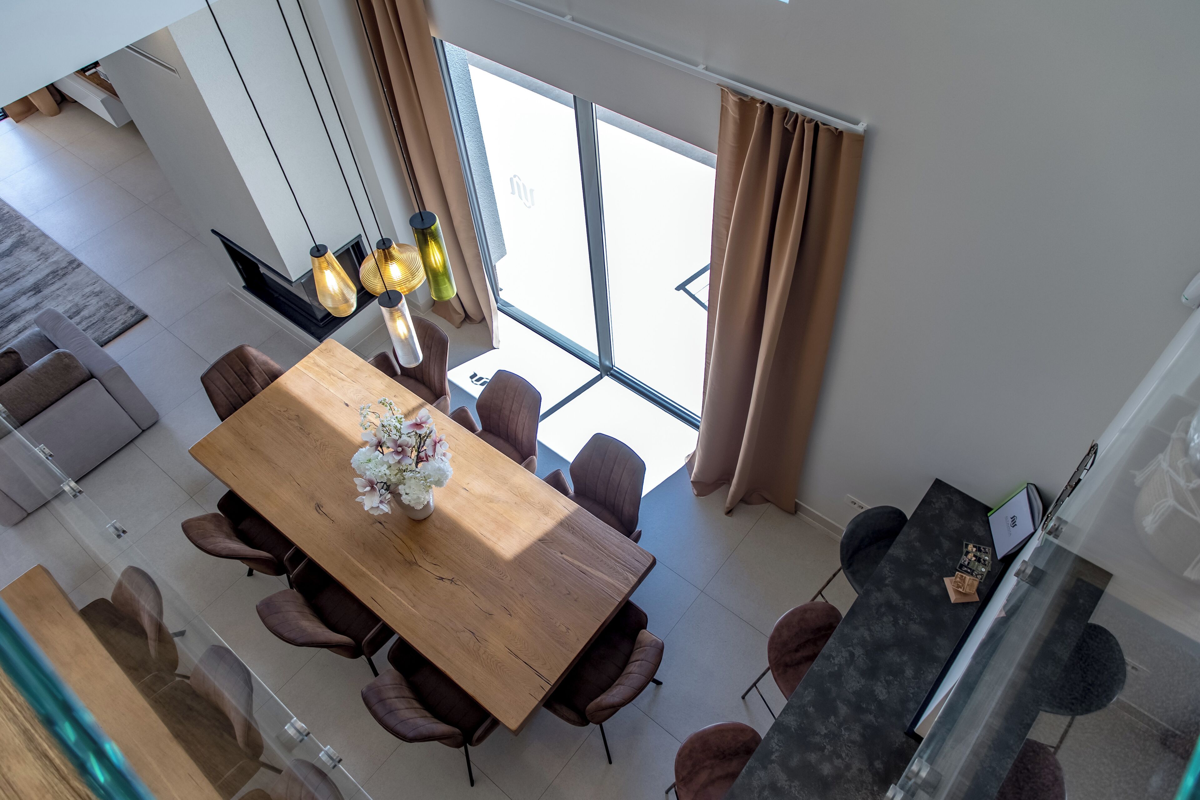 A modern dining area with a wooden table and chairs, large windows, and a view of the outside.