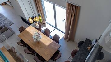 A modern dining area with a wooden table and chairs, large windows, and a view of the outside.