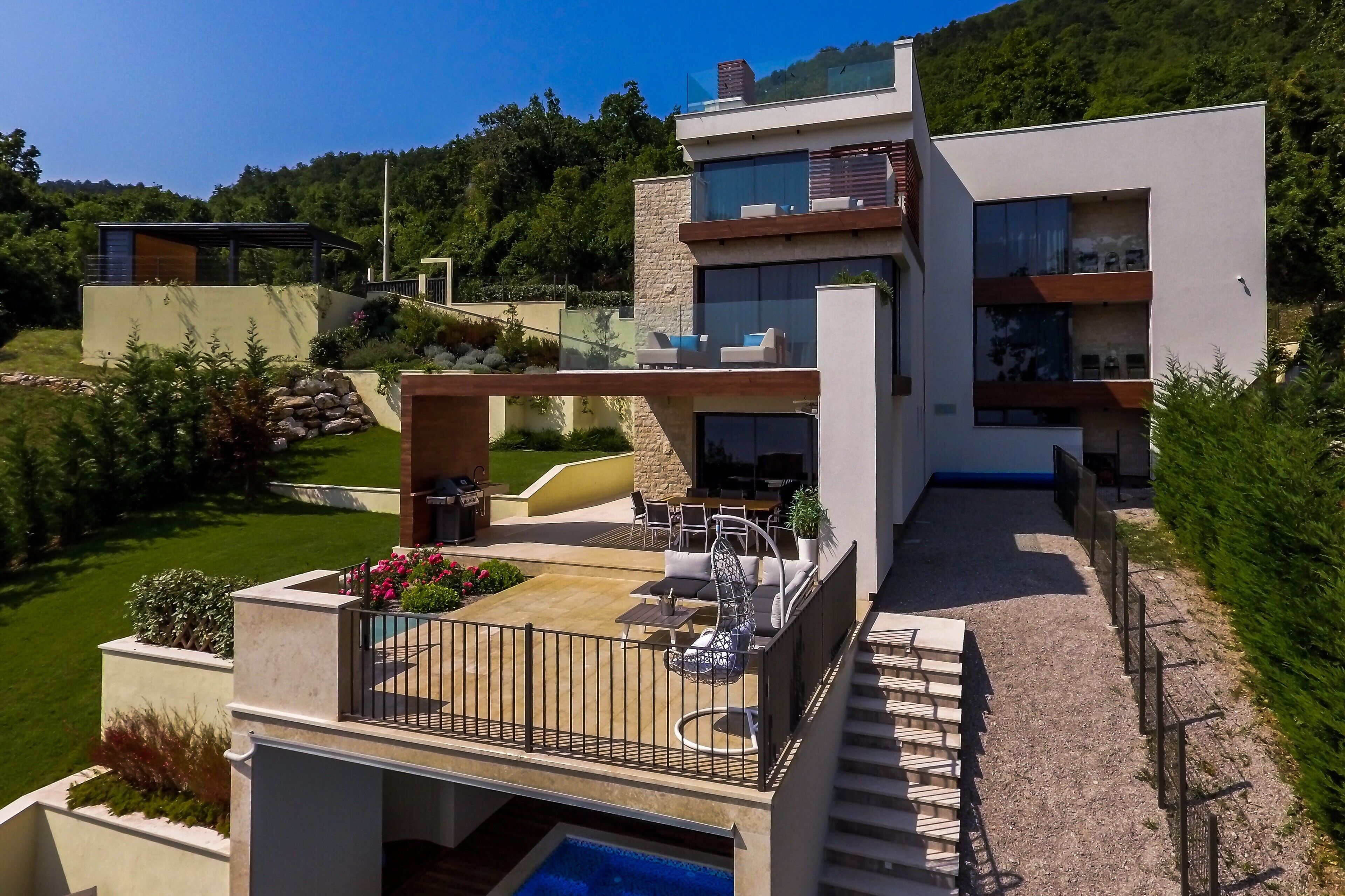 A modern multi-story house with a rooftop patio, outdoor seating, and a swimming pool.