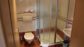 A bathroom with a glass shower enclosure, a toilet, and a sink.