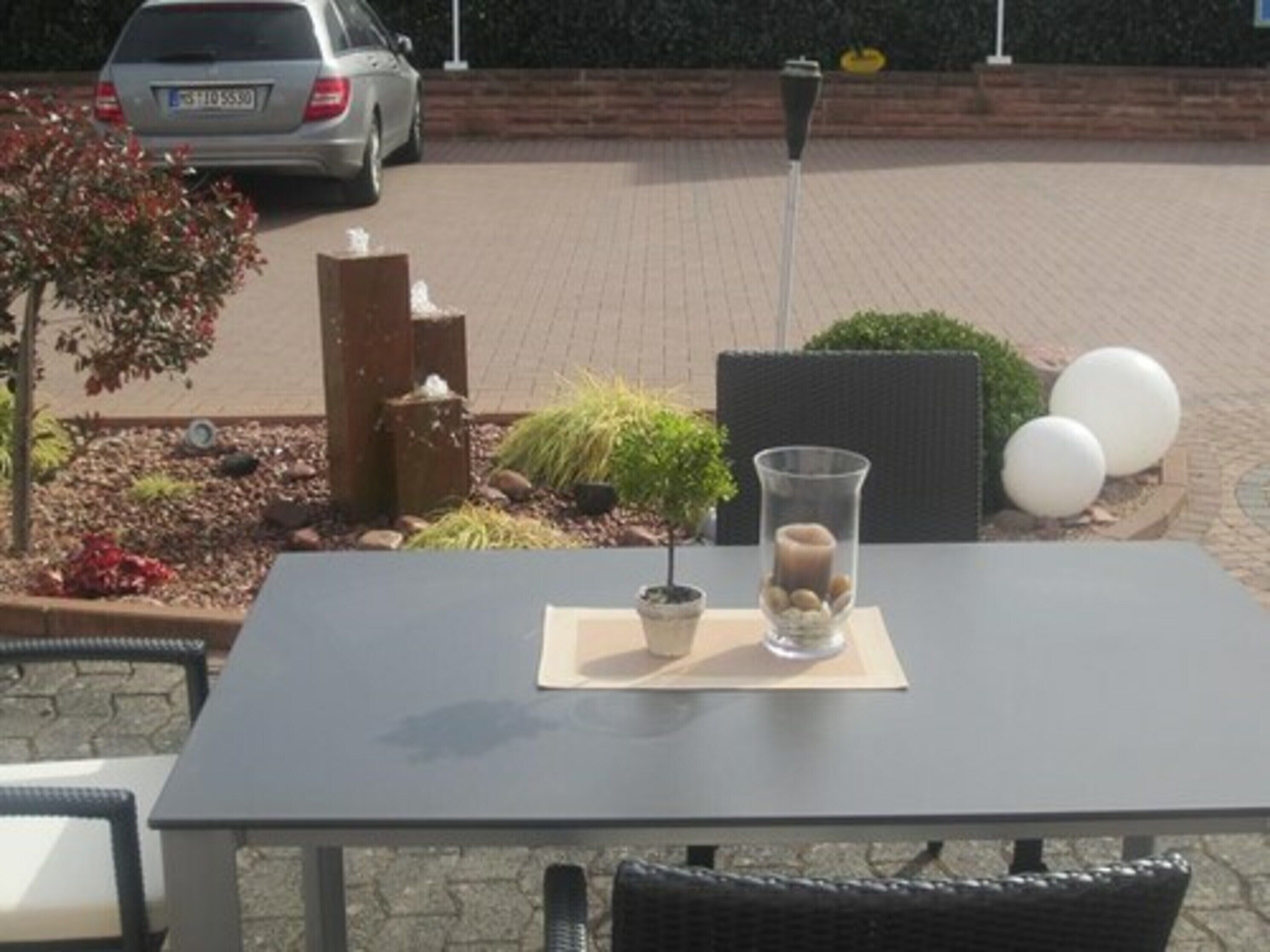 A patio table with a vase of stones and a candle, surrounded by outdoor seating and plants.