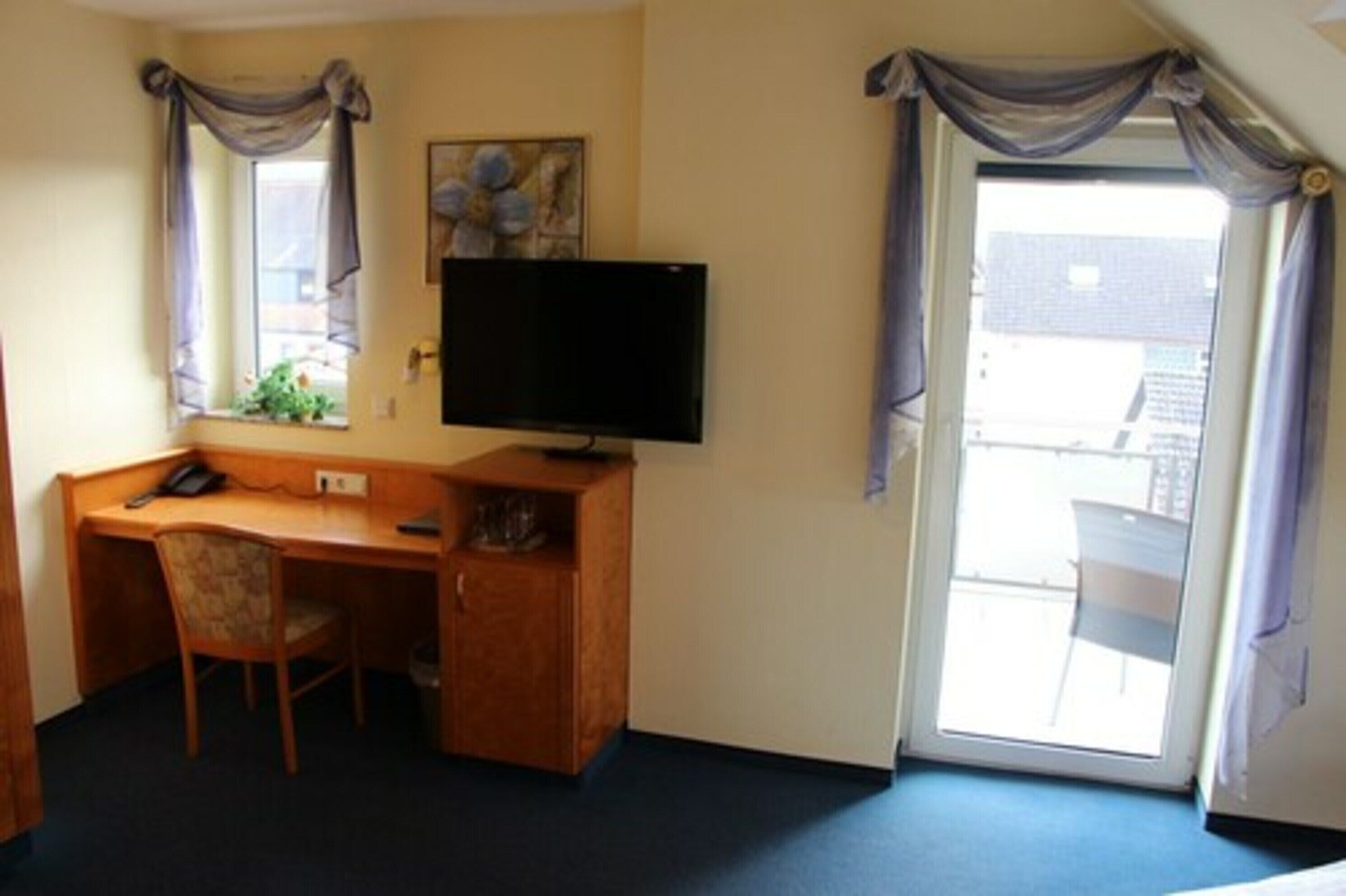Habitación de hotel con escritorio de madera, una silla, televisión de pantalla plana y puerta corrediza de vidrio al exterior.