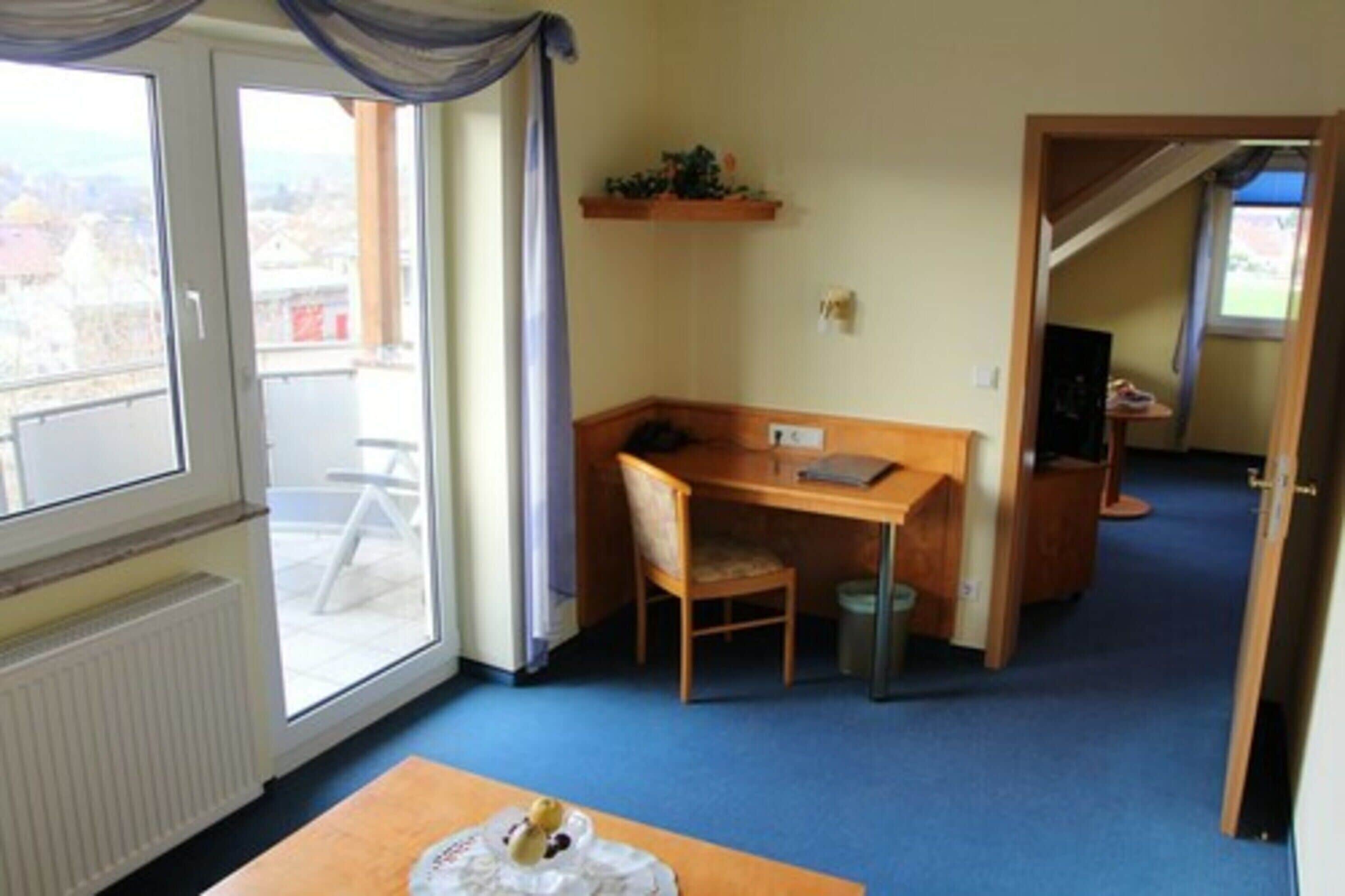 Una habitación con un escritorio de madera, una silla, un radiador, una ventana con vistas y una puerta que da a otra habitación.