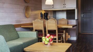A cozy room with a green sofa, wooden dining table, and chairs. A fruit bowl is on the table.