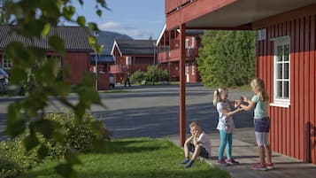 En rød bygning med balkon, græsplæne og vej i baggrunden.