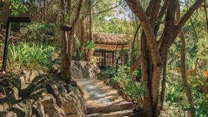 A stone staircase leading to a traditional thatched-roof building surrounded by lush greenery and bamboo. - Vivere Azure (Mabini)