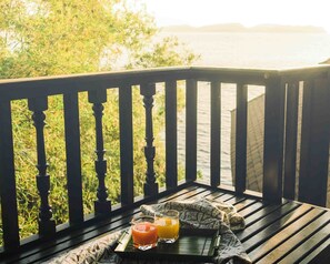 A wooden bench with a tray holding two glasses of orange juice and a bottle, overlooking a body of water and greenery.