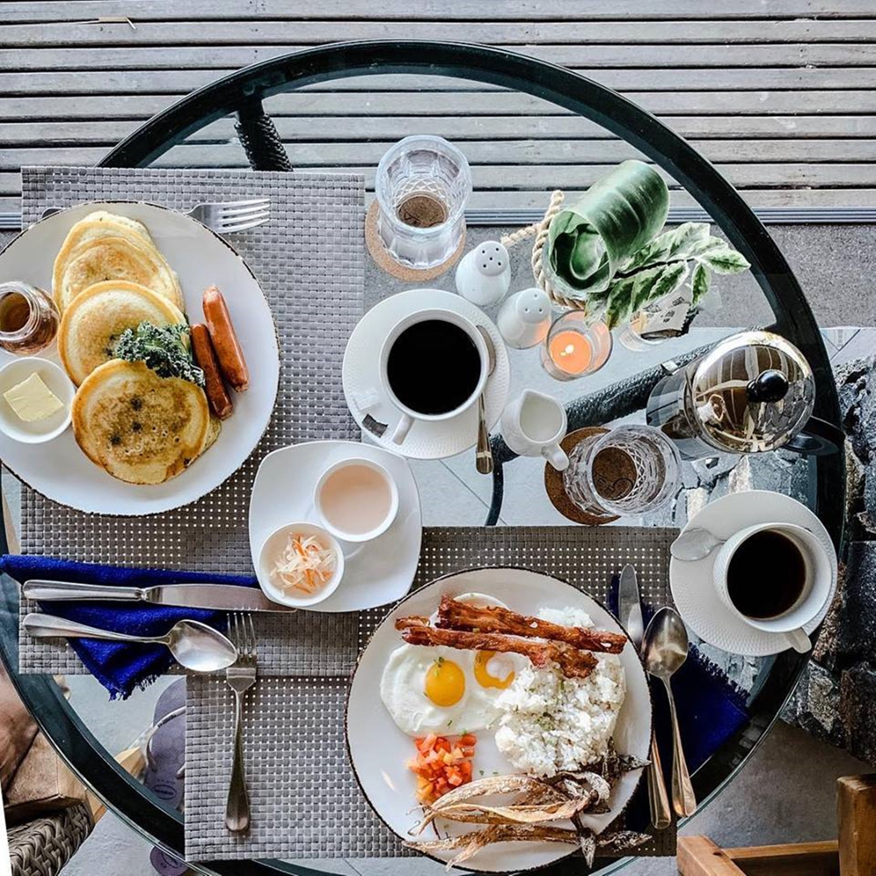 A breakfast setup with pancakes, sausages, eggs, and coffee on a round table.