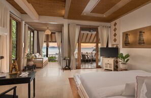 A bedroom with a large bed, a desk, a TV, and a balcony with a view of the sea.