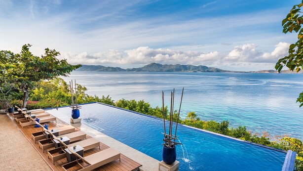 A infinity pool with wooden deck seating and a view of the ocean. - Vivere Azure (Mabini)