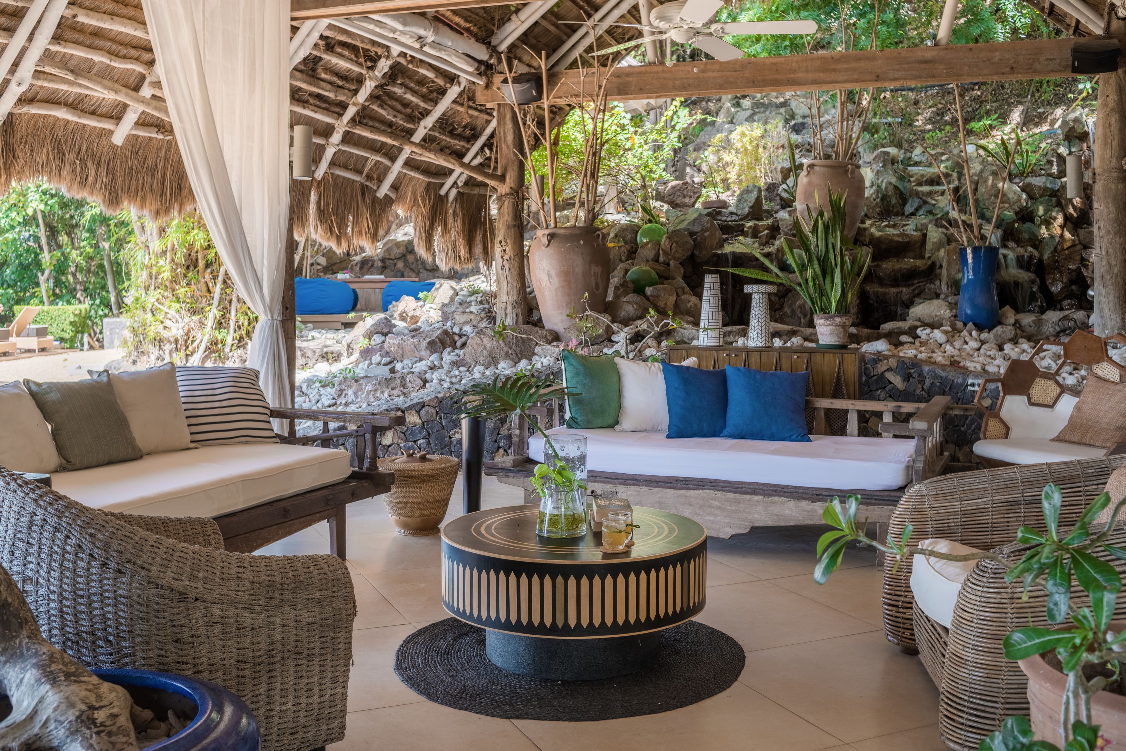 A cozy outdoor seating area with wicker furniture, a round coffee table, and a thatched roof.