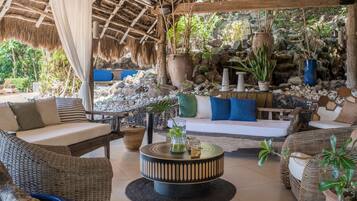 A cozy outdoor seating area with wicker furniture, a round coffee table, and a thatched roof.