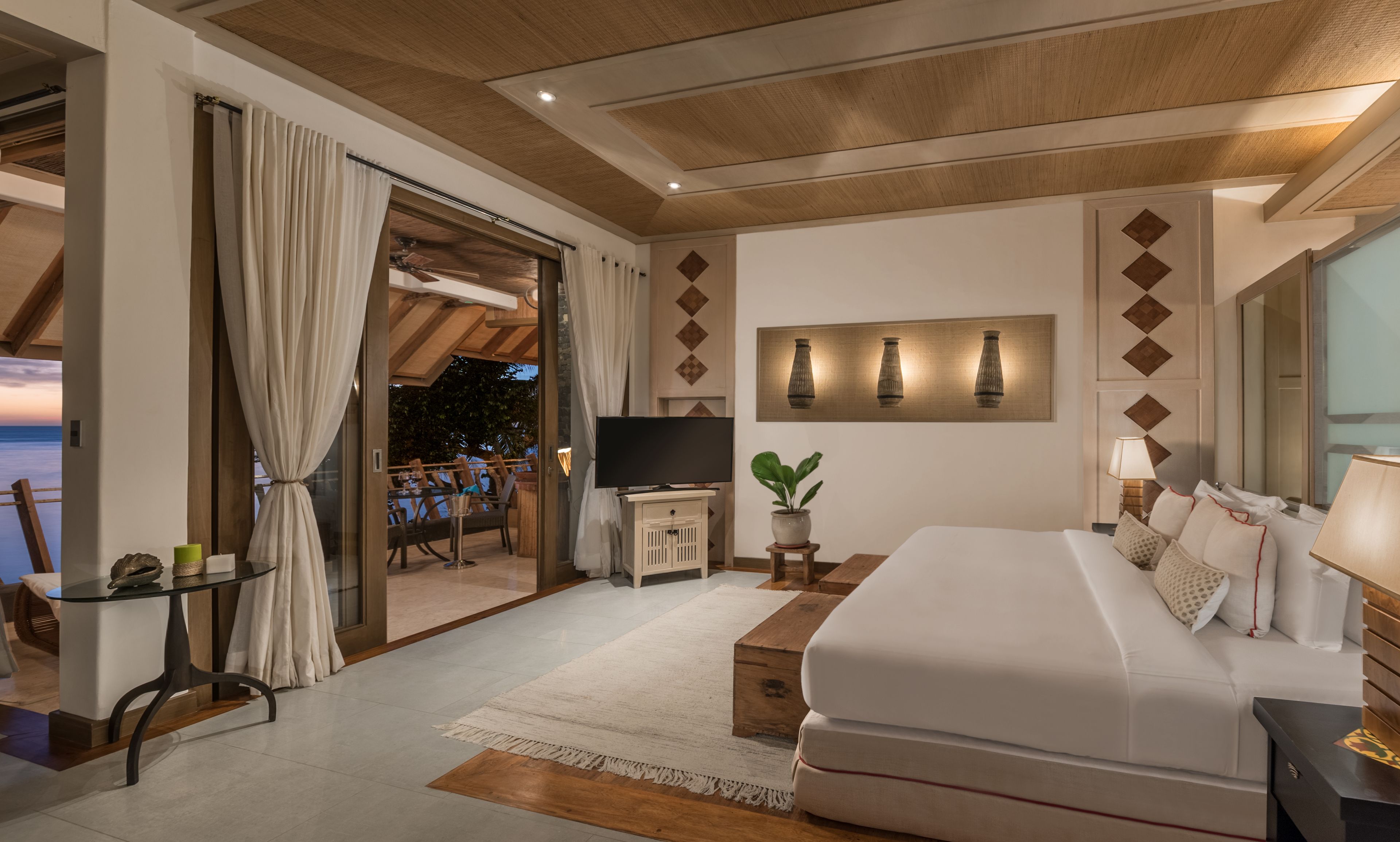 A modern hotel room with a large bed, a TV, a dining area with a view, and a balcony.