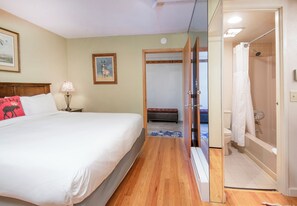 A hotel room with a bed, a nightstand, a lamp, a framed picture, and a view into the bathroom.