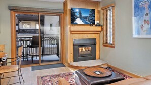 Ein gemütliches Wohnzimmer mit Kamin, einem darüber montierten Fernseher und einer Schiebeglastür, die auf einen Balkon führt.