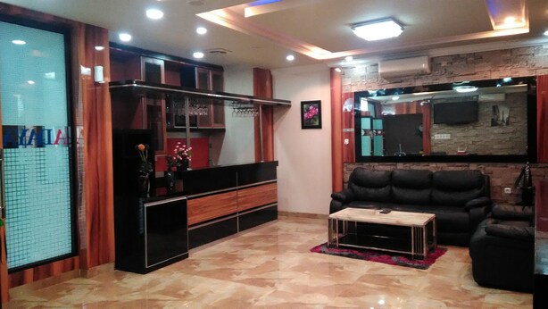A modern living room with a black leather sofa, a wooden coffee table, and a TV mounted on a brick wall. - Adaya Hotel (Bekasi)