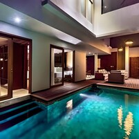 Un espace piscine intérieur moderne, offrant une vue dégagée sur le bassin, avec une terrasse en bois et un coin salon comprenant un canapé et une table.