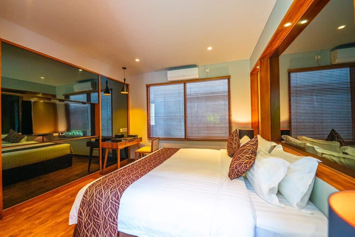 A hotel room with a large bed, a desk, a chair, a mirror, and a window with blinds.