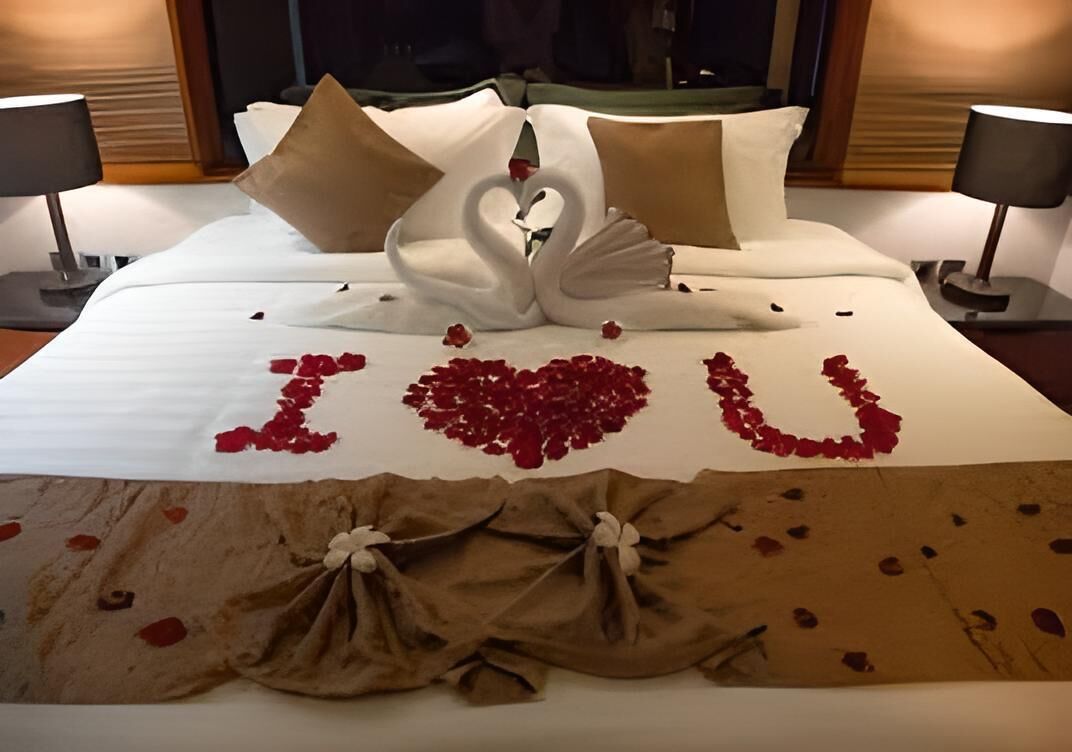 A bed with a swan and heart-shaped rose petals spelling "I love you" and a brown cloth tied at the foot.