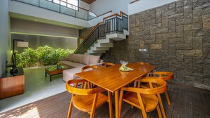 A spacious living area with a wooden dining table, comfortable seating, a staircase, and a stone wall. - Agranusa Signature Villa (Nusa Dua)