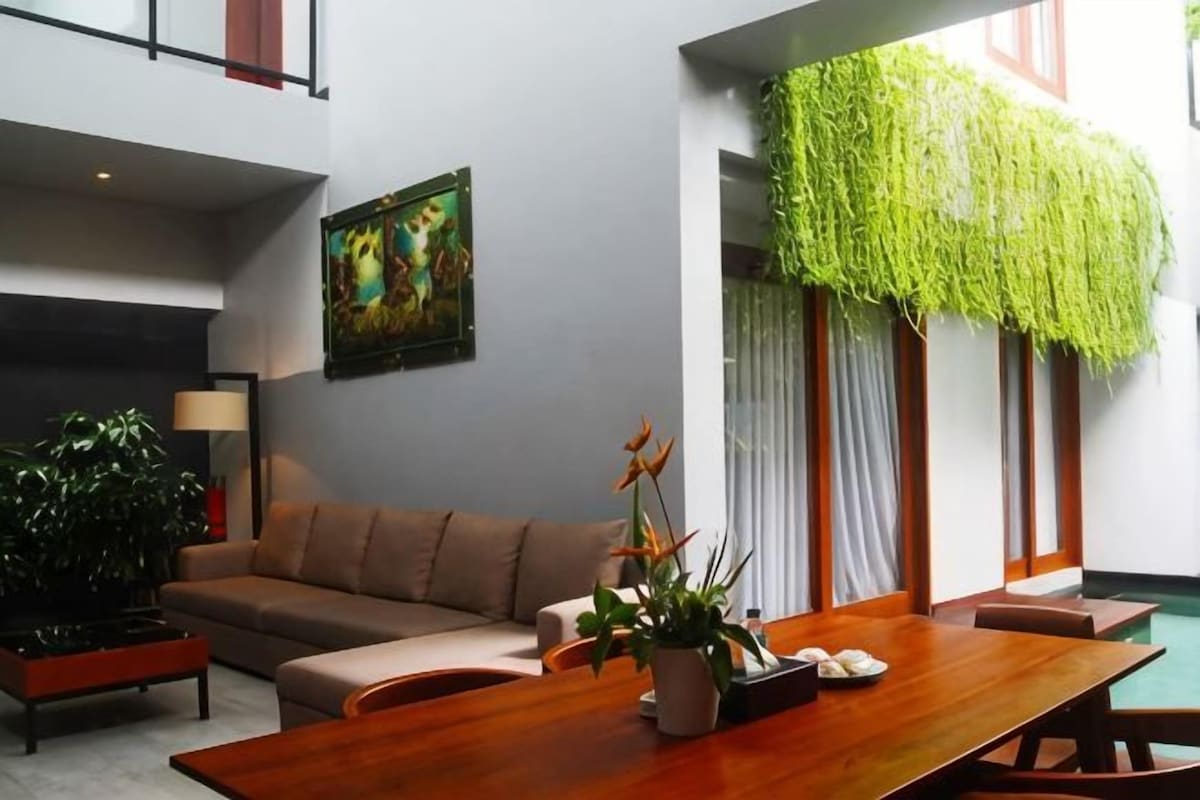 A modern living room with a sofa, a wooden dining table, and a potted plant.