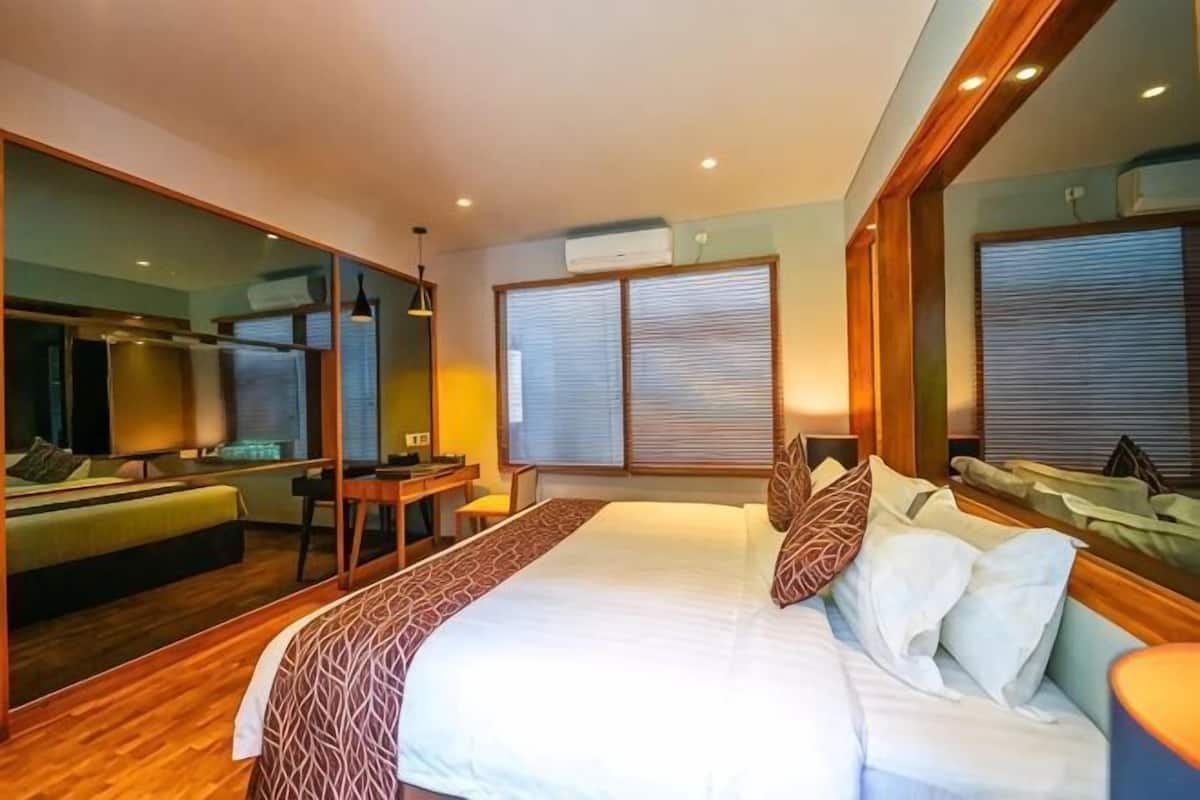 A bedroom with a large bed, a desk, a mirror, and a view of the outside.