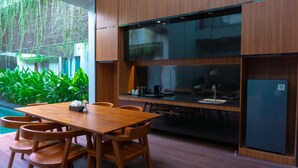 A modern kitchen with a wooden table and chairs, a built-in oven, and a refrigerator. - Agranusa Signature Villa (Nusa Dua)