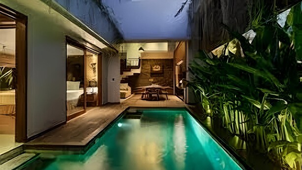 A modern indoor pool area with a wooden deck, a seating area with a table and chairs, and lush green plants. - Agranusa Signature Villa (Nusa Dua)