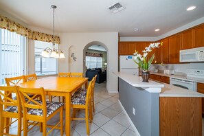 A modern kitchen with wooden cabinets, a white microwave, and a dining area with a wooden table and chairs.