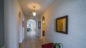 Un pasillo con suelo de baldosas, una mesa roja con un florero y un espejo enmarcado en la pared.
