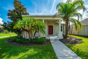 A single-story house with a red door, surrounded by a well-maintained lawn and palm trees.