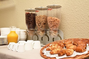 Ein Frühstücksbuffet mit Kaffee, Müsli und Gebäck, sowie ein Korbwicker-Korb mit Croissants.