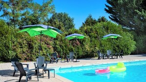 Een zwembad met groene parasols, ligbedden en opblaasringen.
