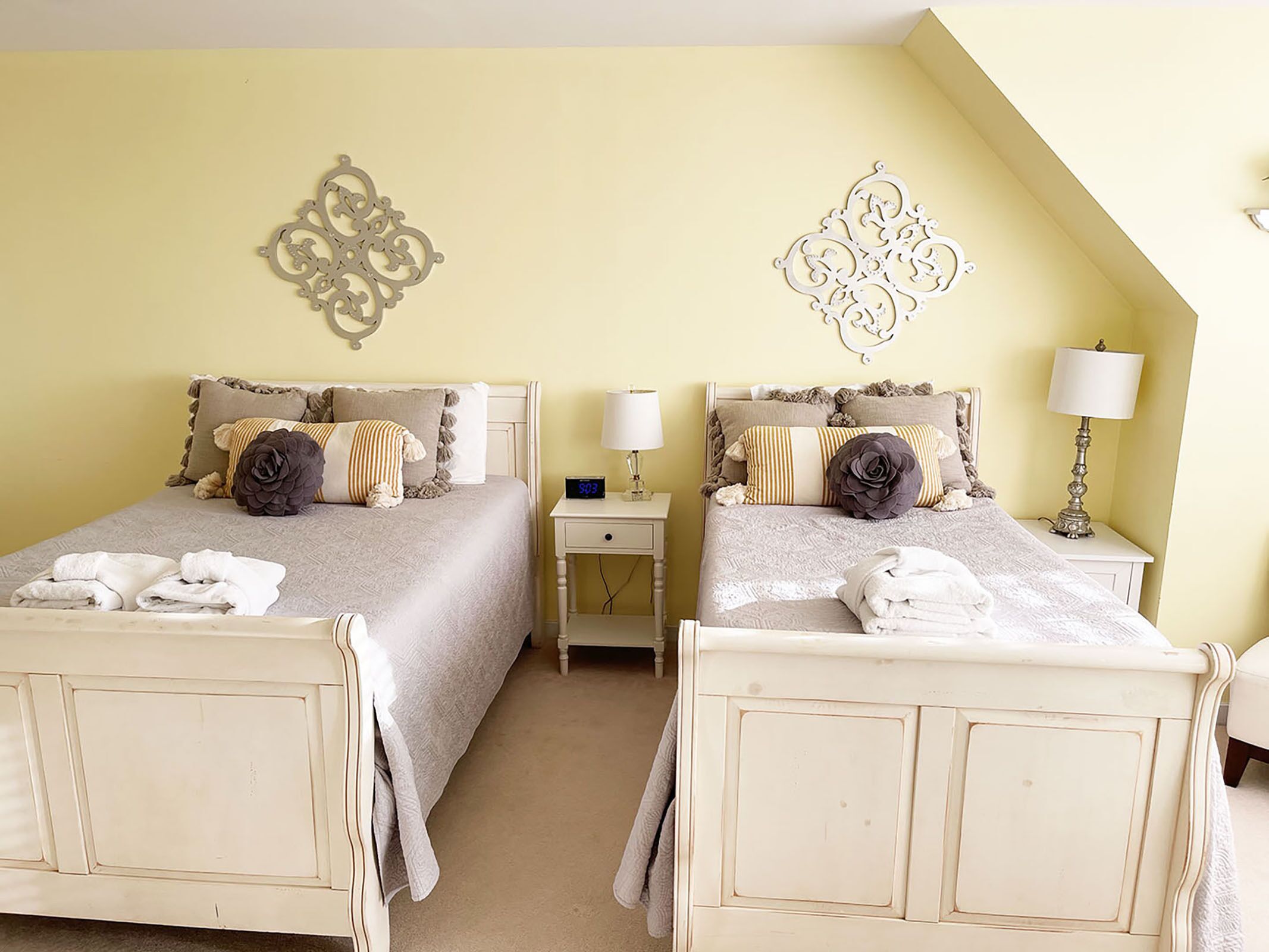A room with two beds, each with a nightstand, a lamp, and decorative wall art.
