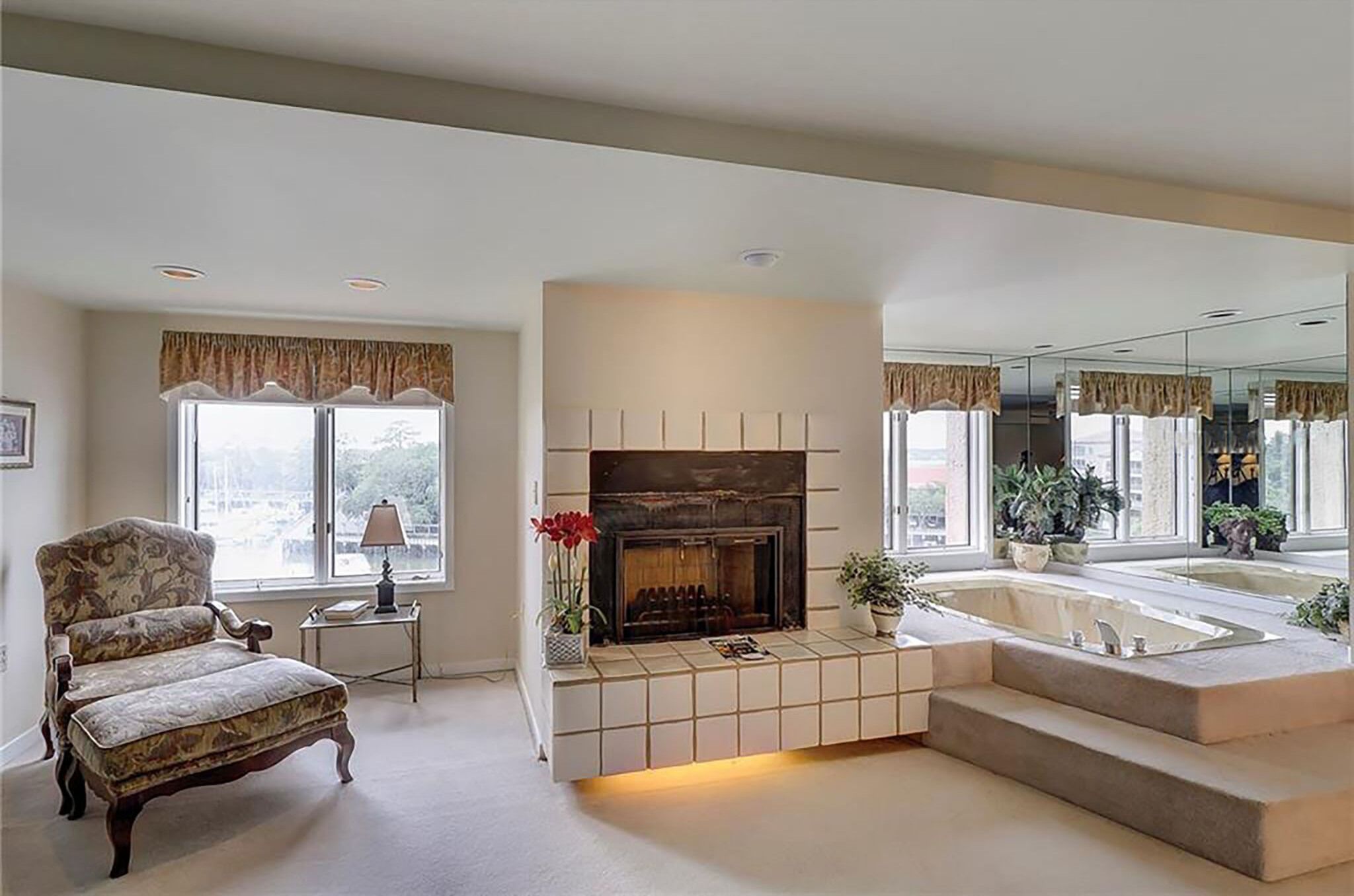 A living room with a fireplace, a large window, a chair, and a bathtub.