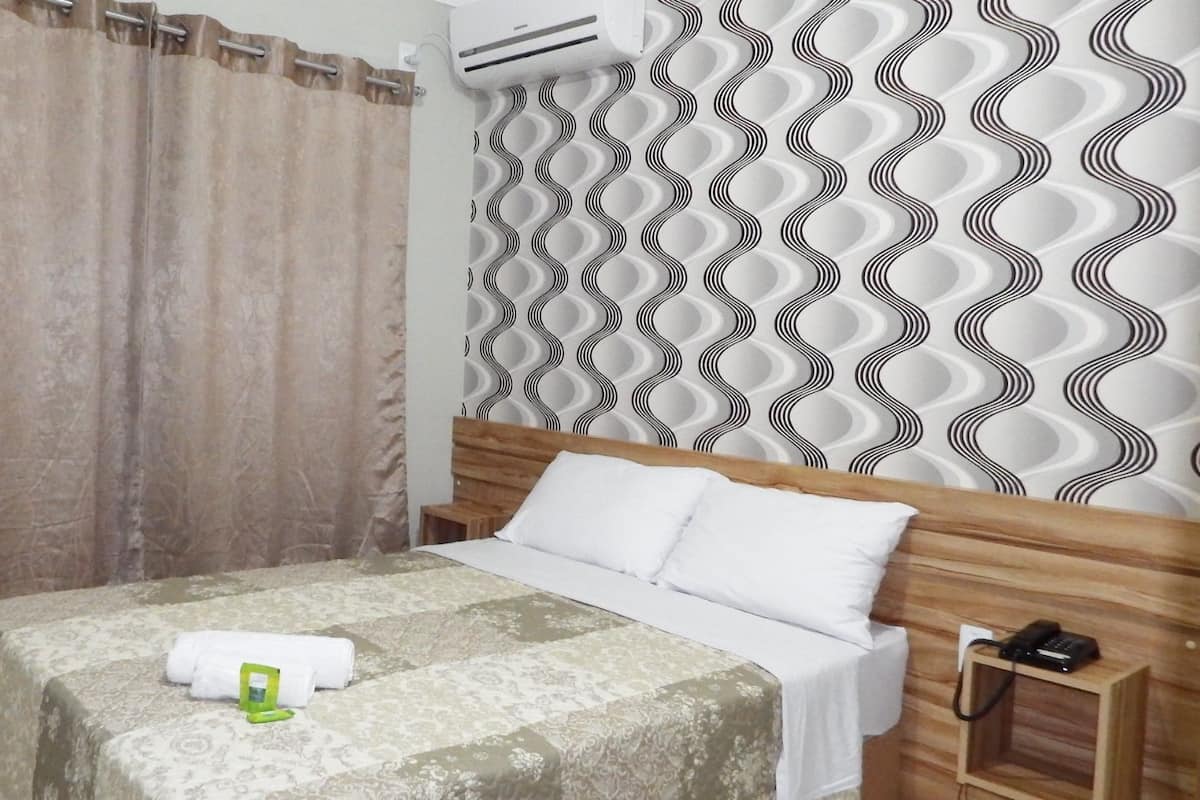 Une chambre d’hôtel avec un lit, une tête de lit en bois, un mur à motifs et un rideau.