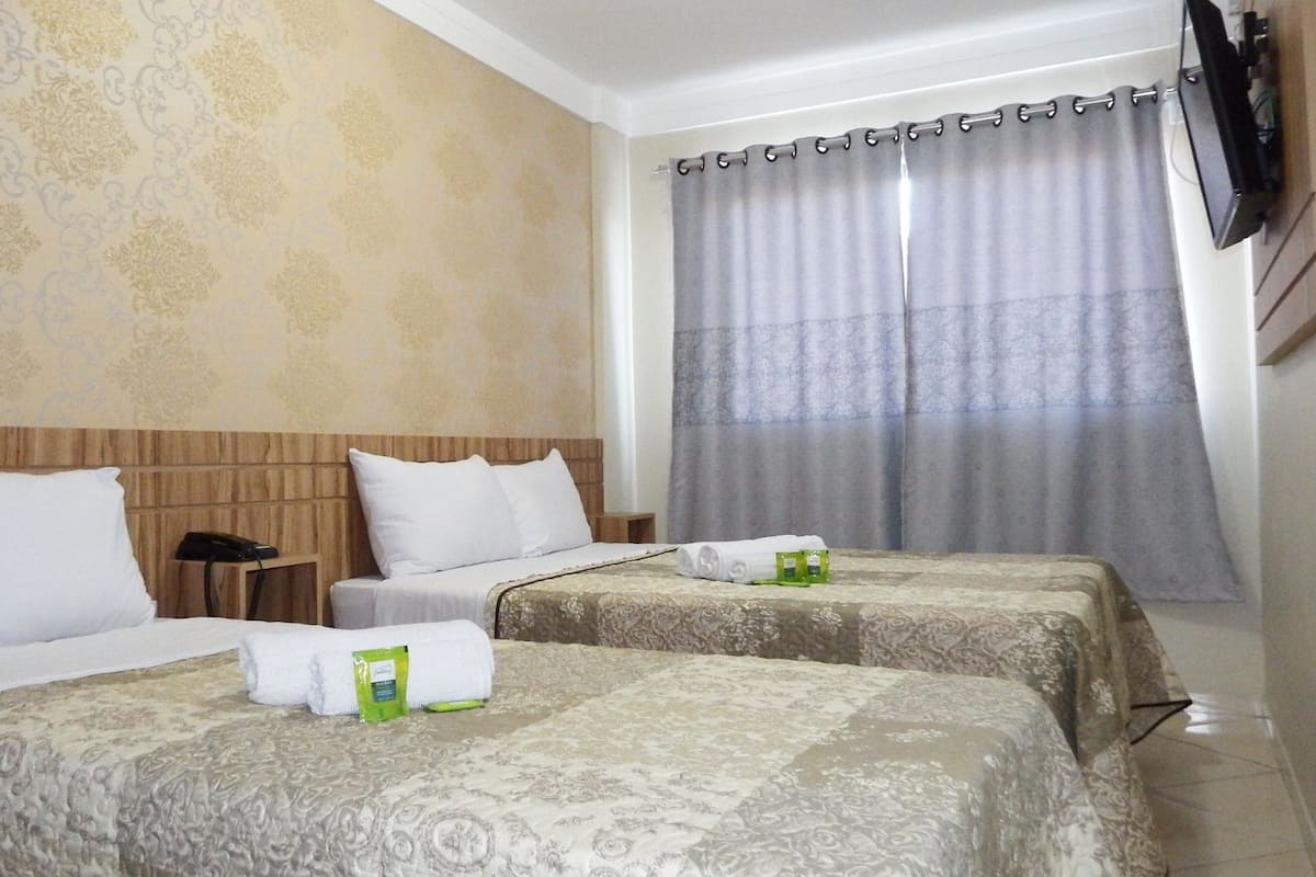 Une chambre d’hôtel avec deux lits, une tête de lit en bois, un téléphone et une fenêtre avec des rideaux.