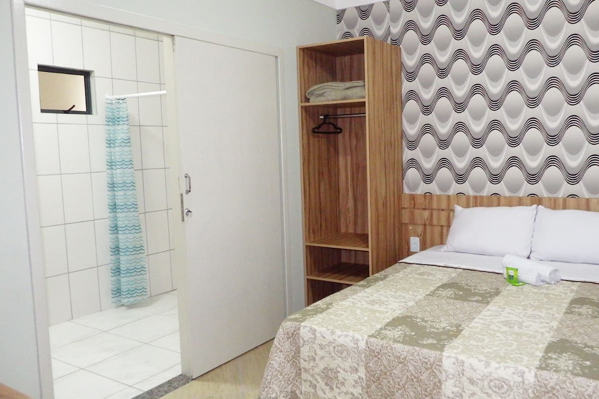 Une chambre à coucher avec un lit, une armoire en bois, une salle de bain avec un rideau de douche et un papier peint à motifs.